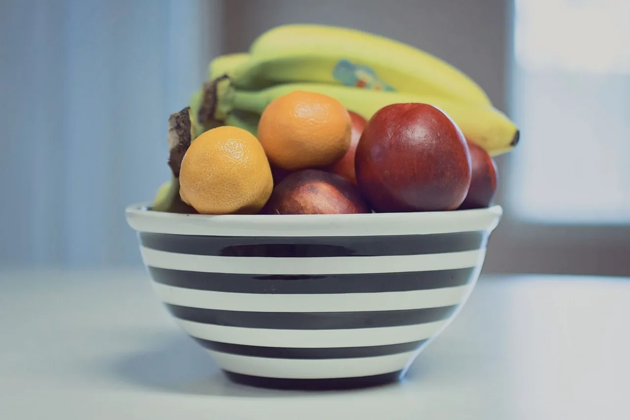 Miska w paski z bananami, cytryną i brzoskwiniami na kuchennym blacie