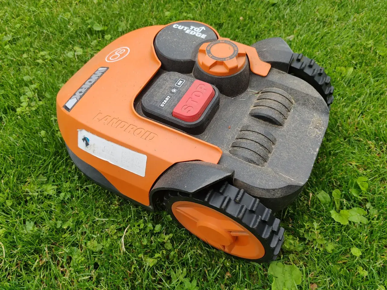 Zakurzony robot koszący na trawniku po sezonie, przed czyszczeniem i odstawieniem na zimę